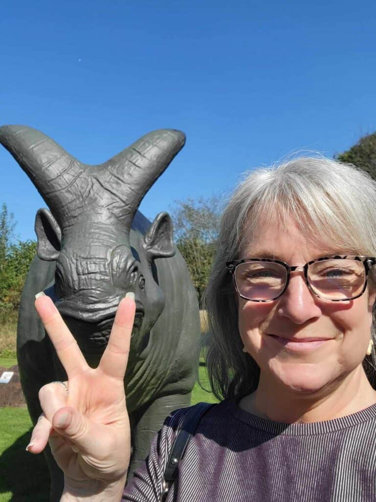 A woman giving the peace sign in front of a dinosaur with a v-shaped horn