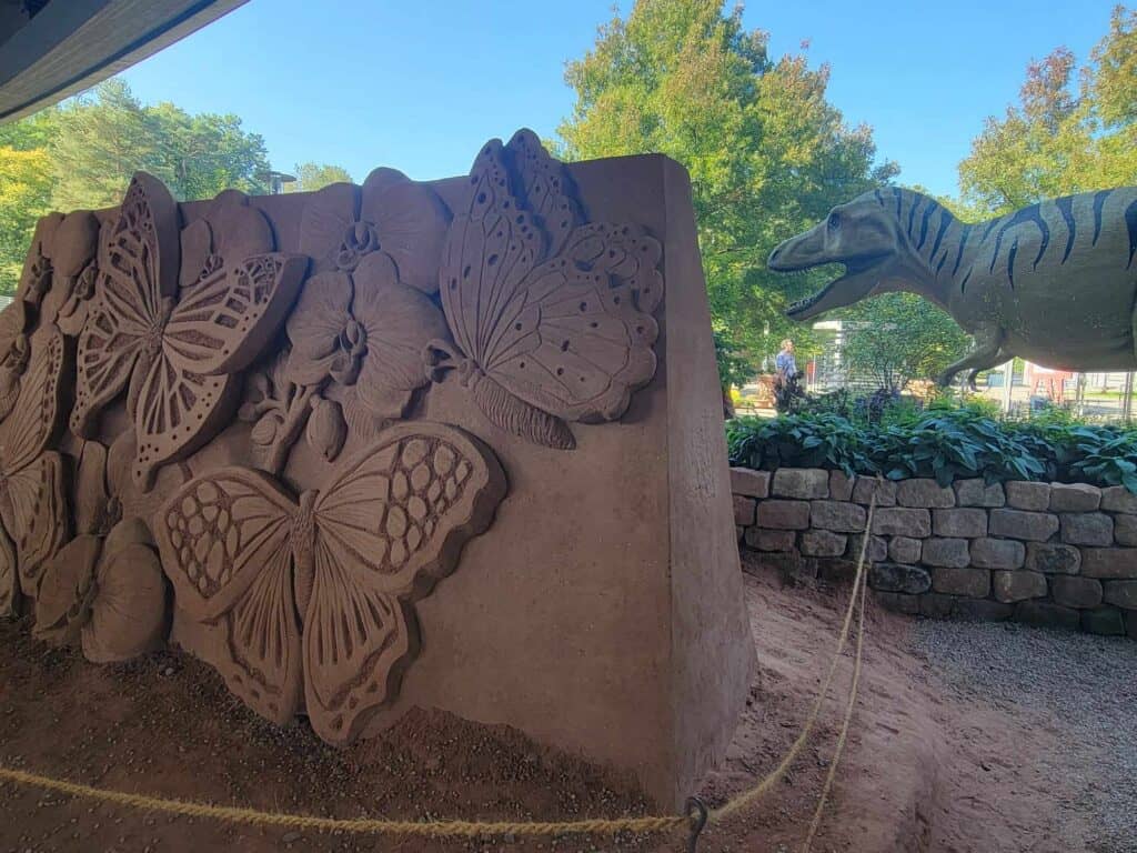 A large panel of red sand with butterfly carvings and a large T-Rex behind