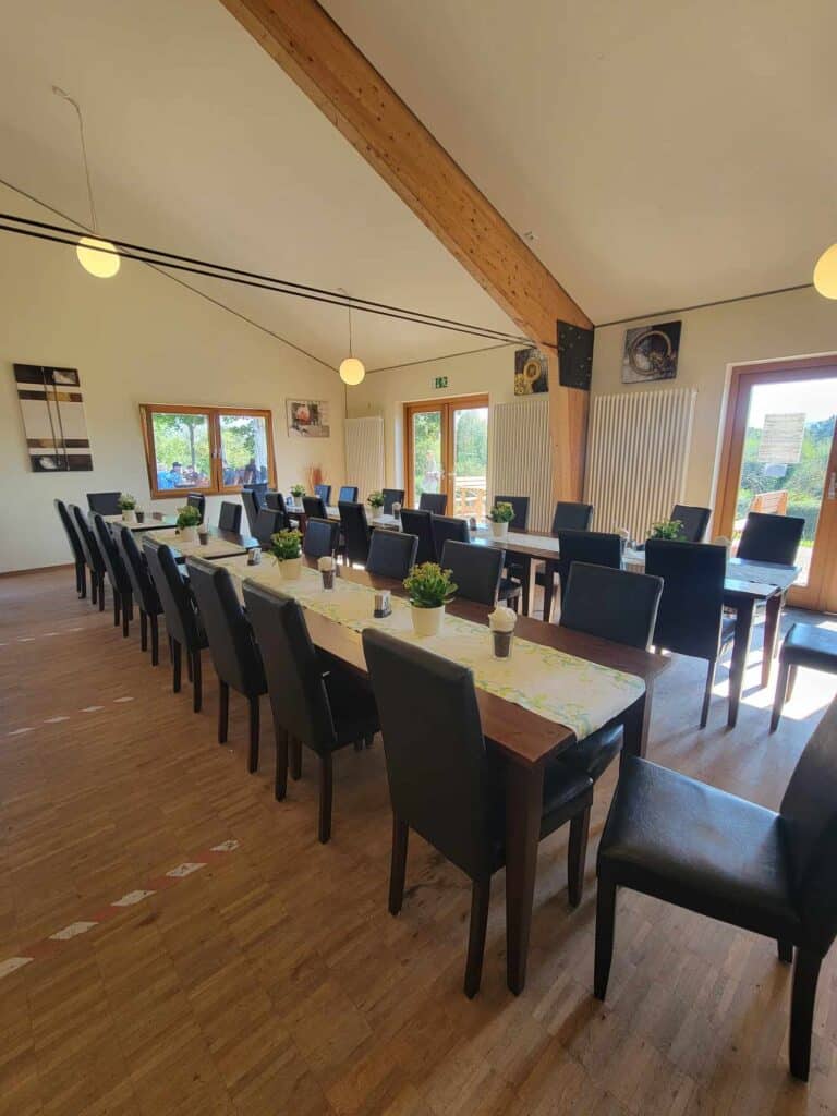 Indoor dining room with long tables and grey chairs with a wooden floor and windows