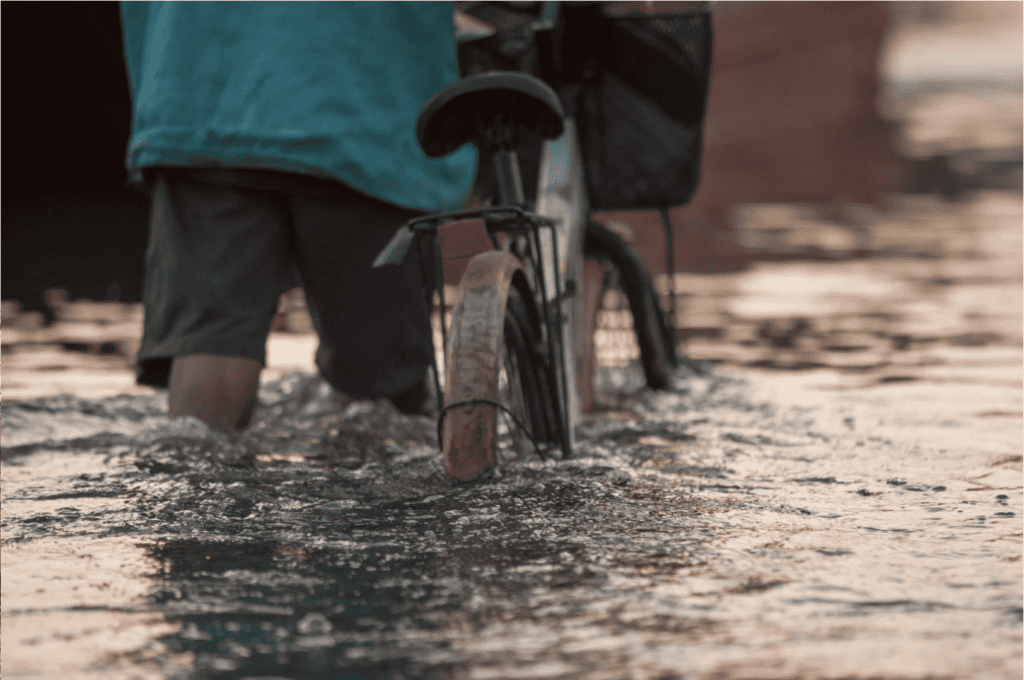 Someone pushing a bicycle through knee-high flood waters