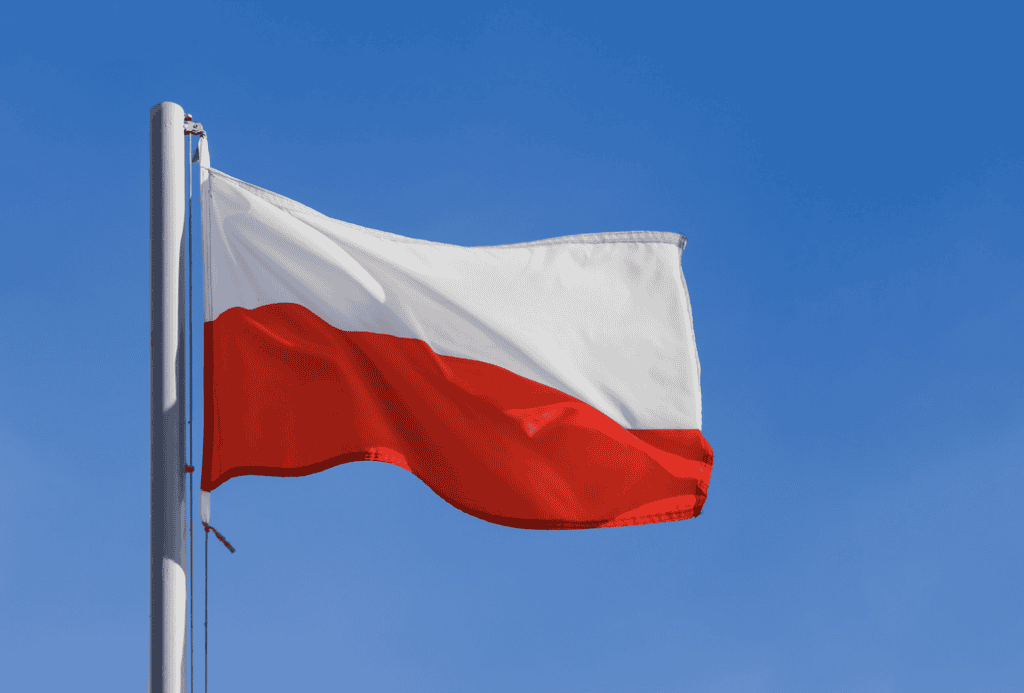 The Polish flag with a white top half and red bottom half flies against a blue sky