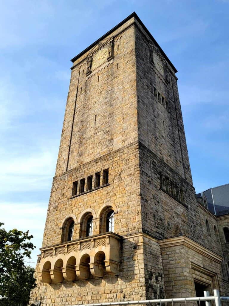 A square clock tower with a flat roof, three arched windows and a balcony.