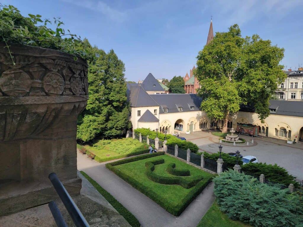 A view of part of the limestone castle with pointed turrets. The lion fountain sits in the courtyard and in front is a manicured formal hedge garden