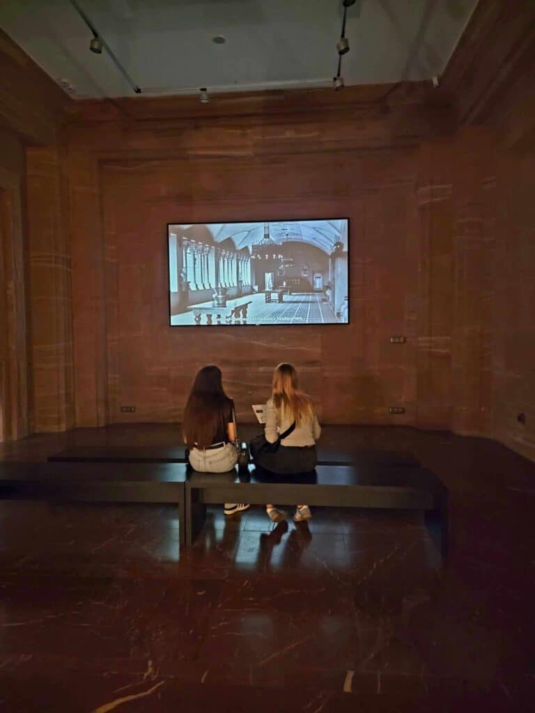 Two woman sitting with their backs to the camera watching an informational film on the Imperial Castle in Poznan