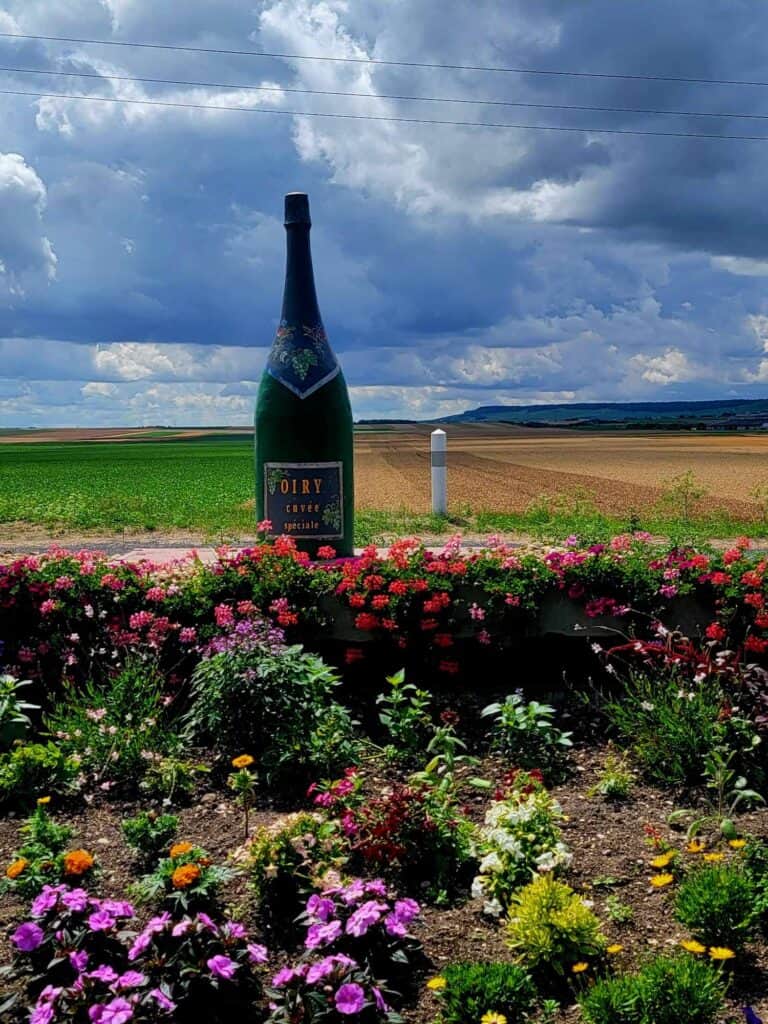 A huge decorative roadside champagne bottle in a colorful flower garden