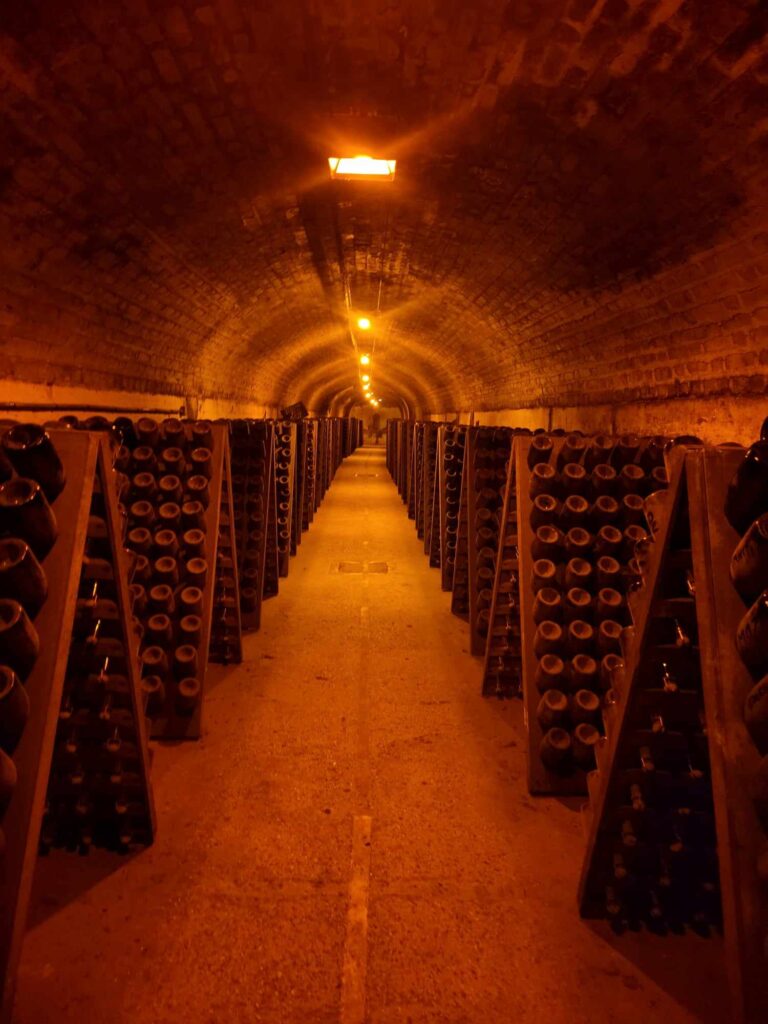 A long cave in orange light with hundreds of champagne bottles in racks