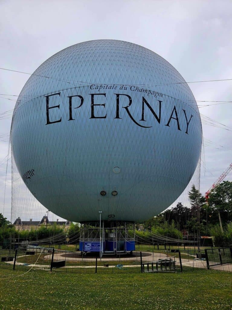 A huge spherical white balloon with a blue carriage underneath and "Capital du Champagne EPERNAY" on it.