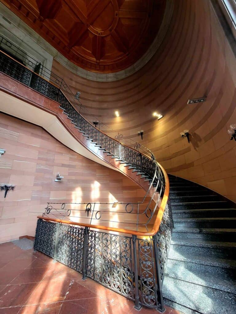 A tall and sweeping black granite curved staircase with wrought iron railing topped with a polished wooden handrail