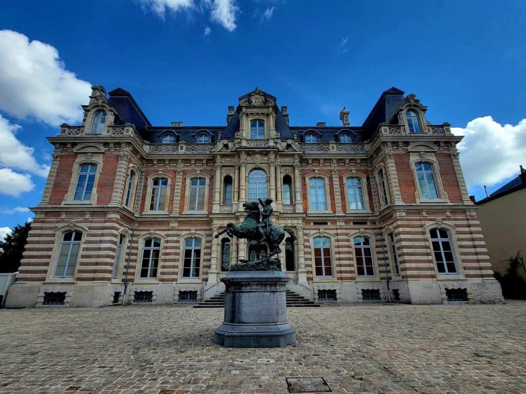 The museum of champagne - a red and white stone and brick mansion with a huge bronze statue of a man on a horse sitting on a pedestal