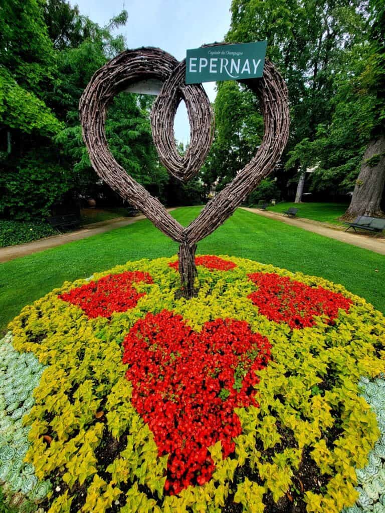 Twisted willow branches in the shape of a heart on a bed of flowers with a green sign reading EPERNAY