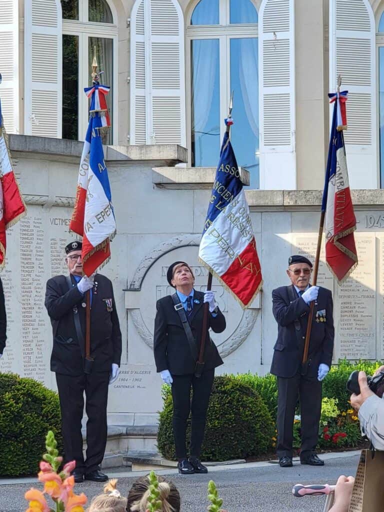 A row of people in uniform carrying the french flag in front of a white marble WWI memorial on July 14th