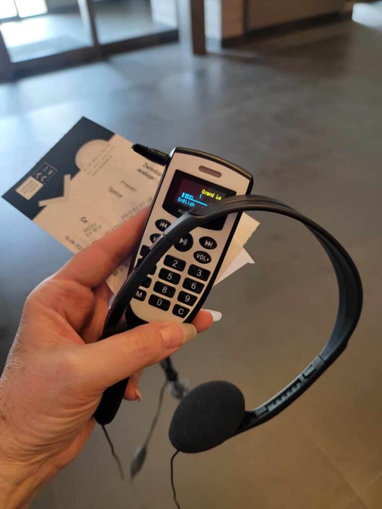 A woman's hand holding an audio guide, a set of headphones, and a ticket