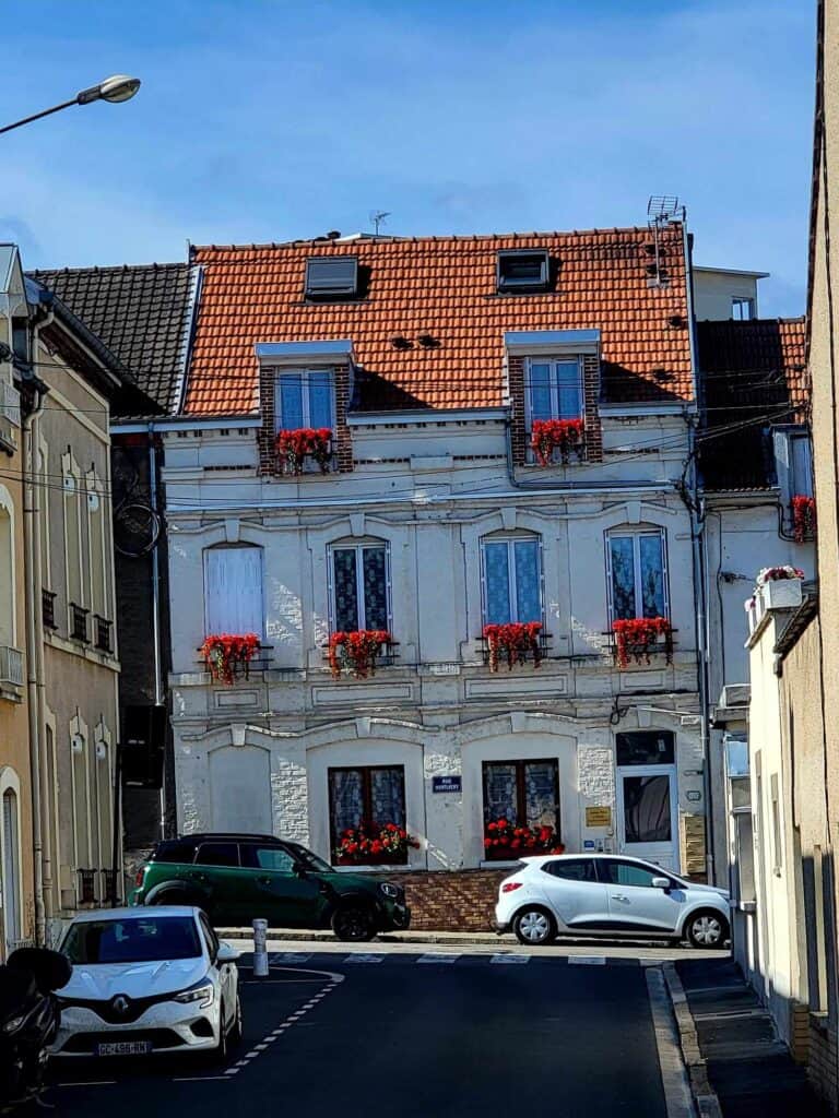 A very french looking urban house with tall windows, a red tile roof, and boxes of red geraniums in the windows