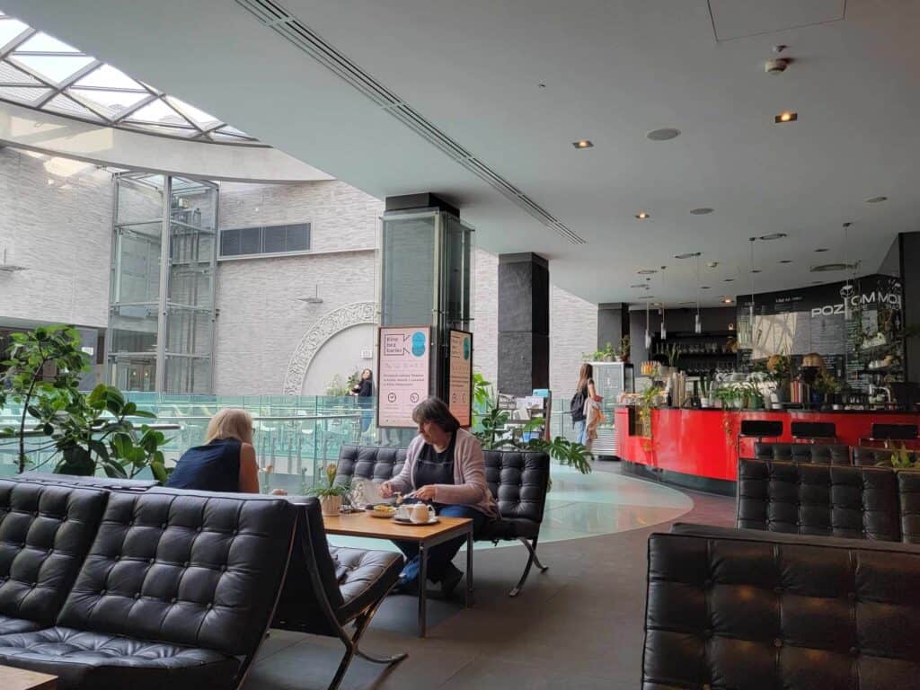 Black leather tufted armless sofas with a low wooden table between, and a red coffee counter with pendant lighting