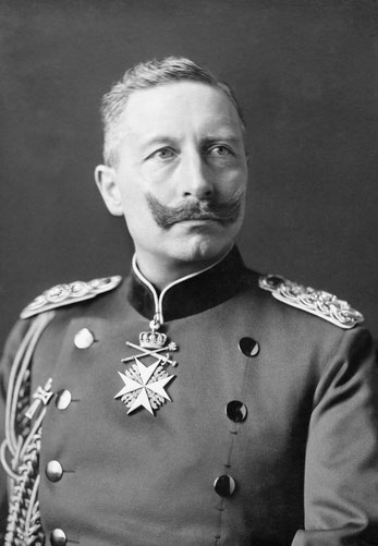 Kaiser Wilhelm II with a dramatic upturned mustache in a military uniform with gold braided epaulets and a large medal topped with a crown in the center of his chest.