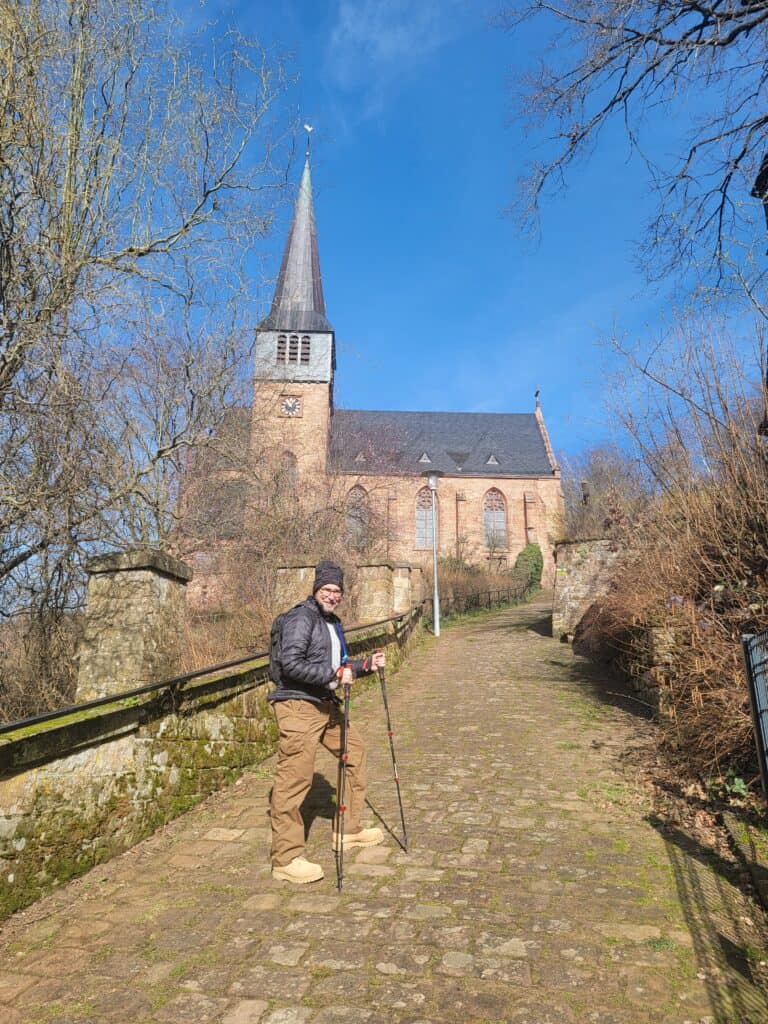 A man with hiking sticks walking up a cobblestone path with a church next to it