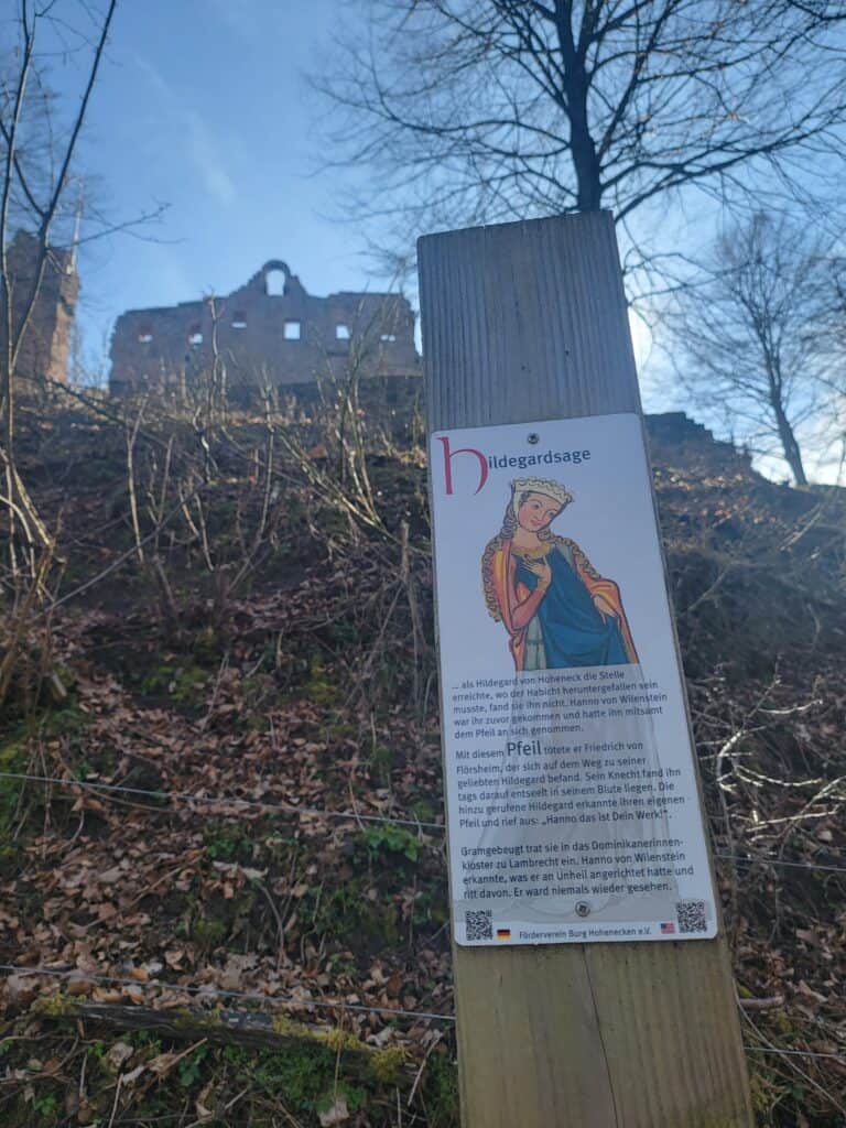 A castle ruin on top of a tall hill and a sign in German telling about it