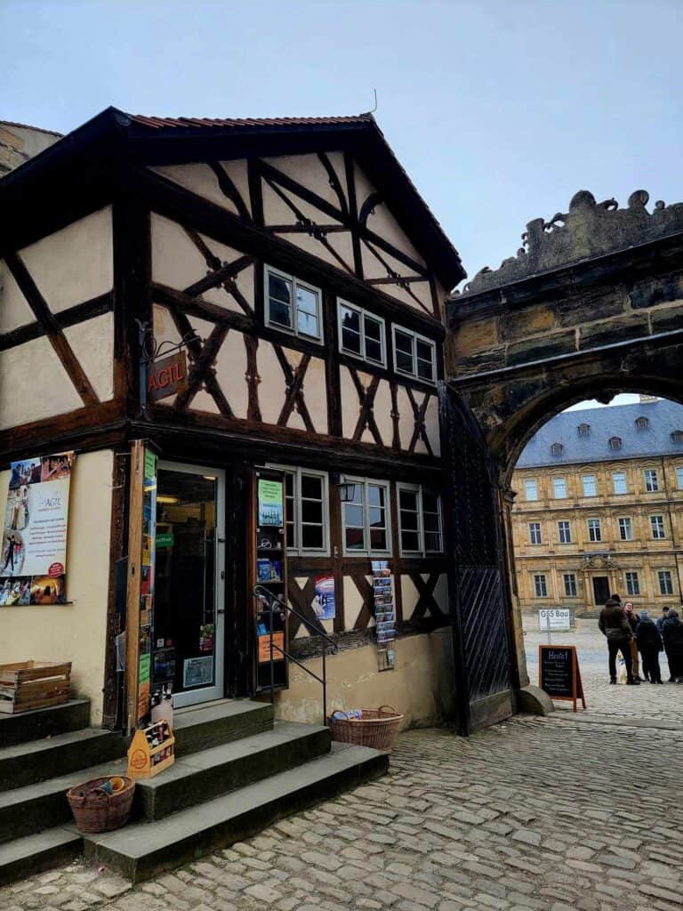 A timbered building with stairs leading to the door and a stone arch on the right