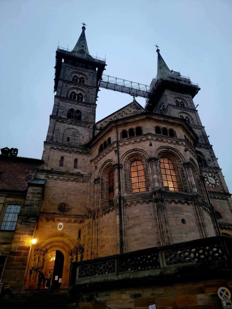 Two towers on a Romanesque bulding with an arched door, illuminated with yellow light from within at dusk