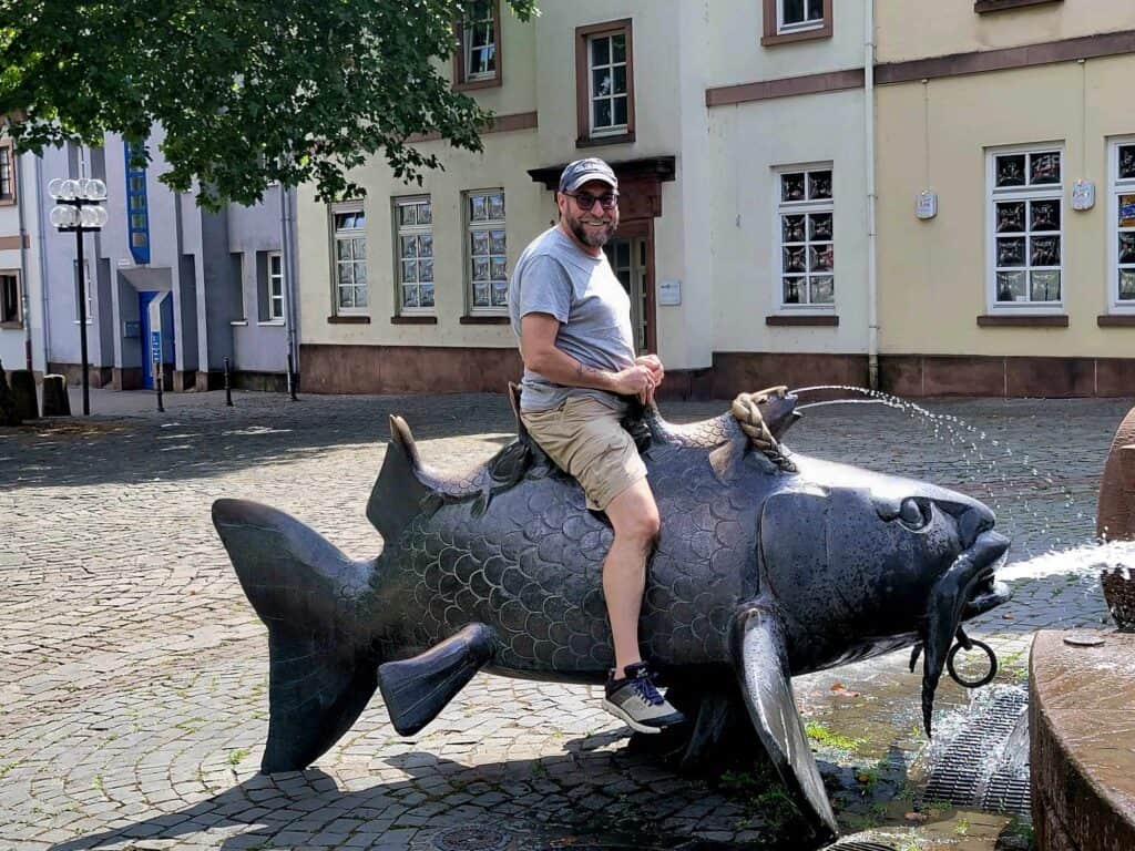 A grown man riding a giant bronze carp next to a fountain