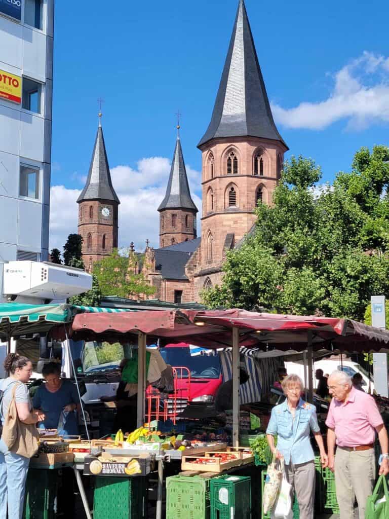 The Stiftskirche in the background and a couple walking by stalls with tables full of fruit