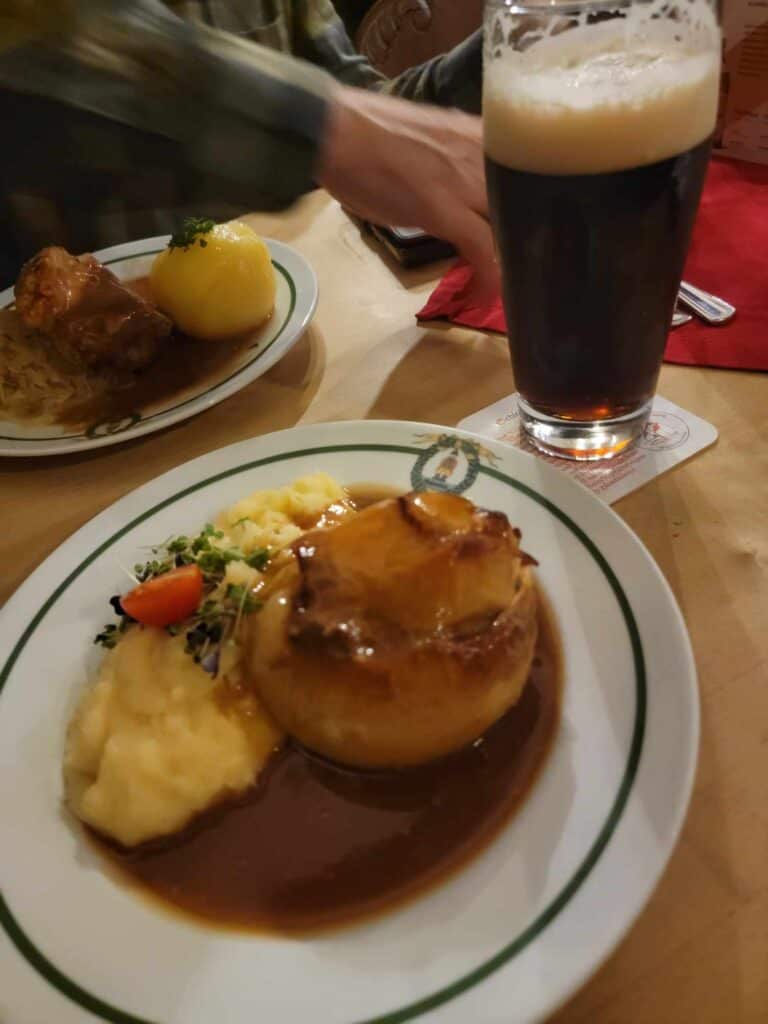 A plate of food featuring an onion and mashed potatoes covered in gravy, and a glass of dark foamy beer