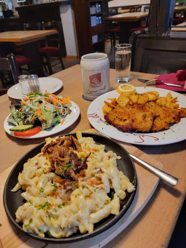 A salad, a schnitzel with fries, an a plate of käse spaetzle with crispy onions