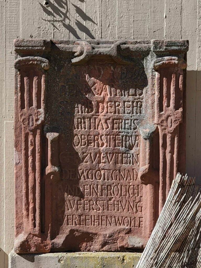 An old grave marker leans against a wall