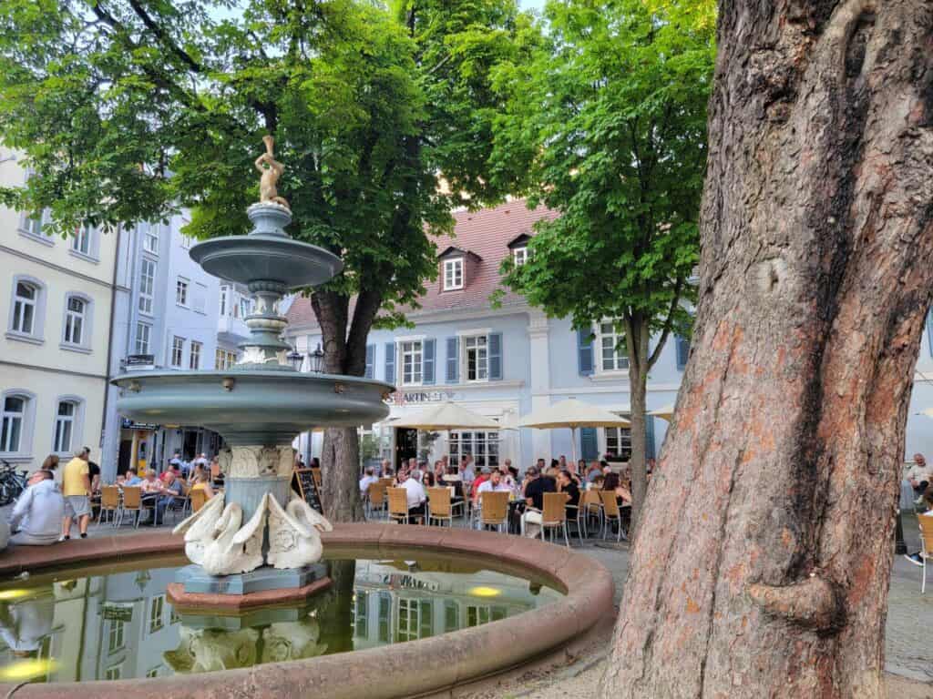 The fountain with tables and umbrellas with people dining behind