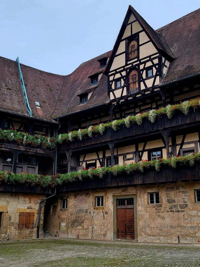 The Old Court courtyard with a tall timbered structure with lots of windows and a walkway decorated with plant boxes