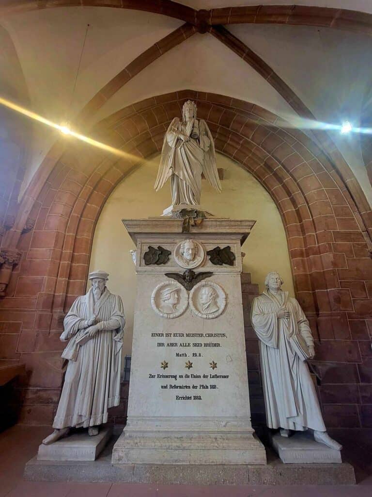 White marble likenesses of Calvin and Luther next to a white marble pediment with an angel on top