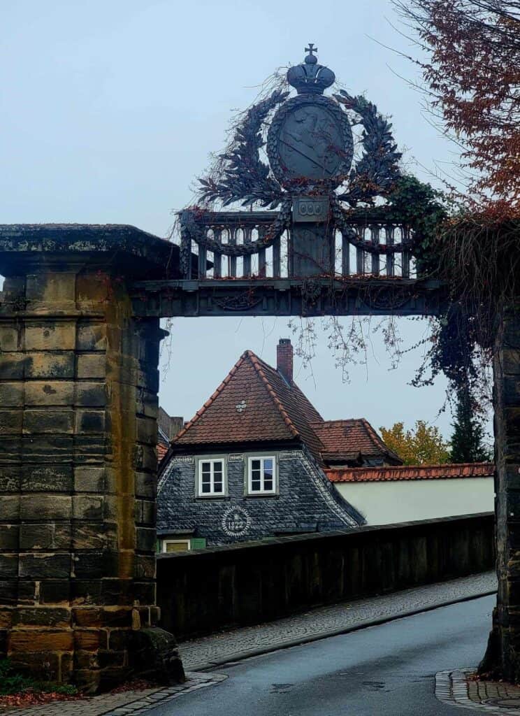 A 19th century building with shingled siding and a pointed roof seen through an arched gate