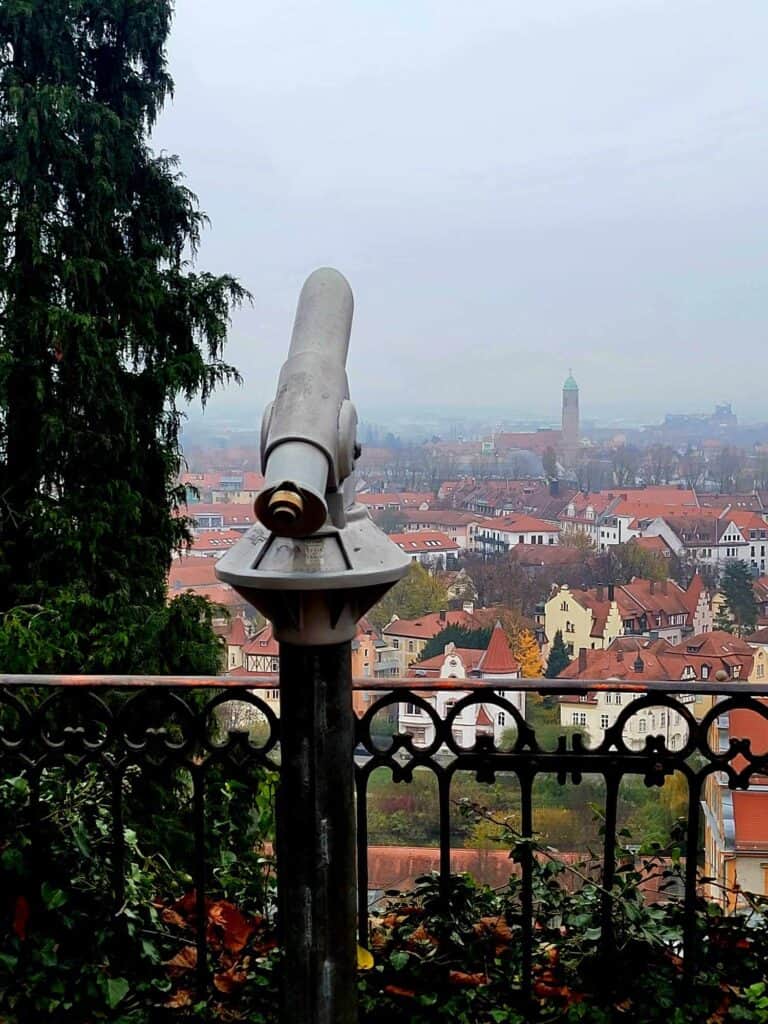 A telescope on a terrace pointed over the city of Bamberg with spires and red roofs