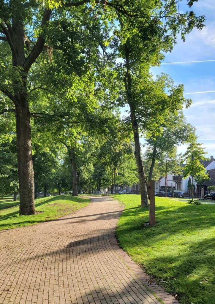 A brick path winds through a green lawn with trees