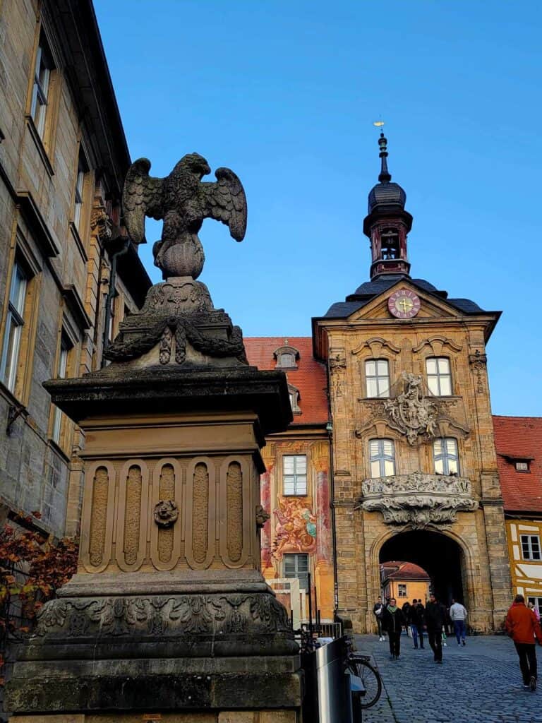 Blue sky with a stone eagle sculpture and a covered tunnel through a building with a clock and a spire