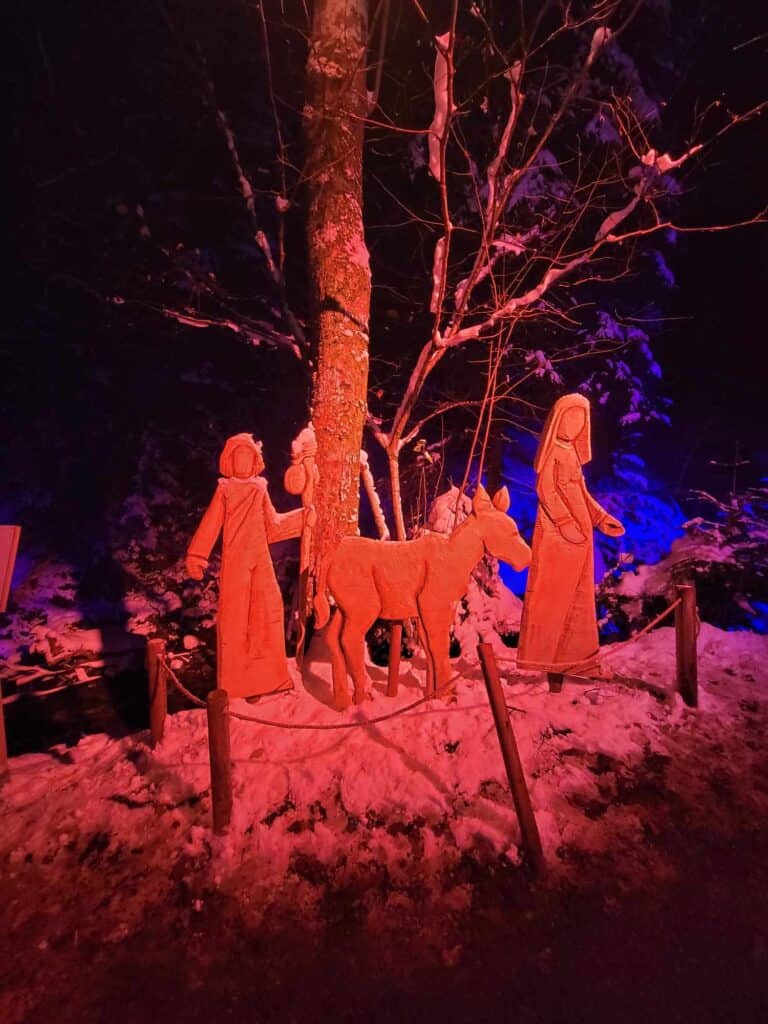 Wooden carving of people walking and a donkey illuminated in red