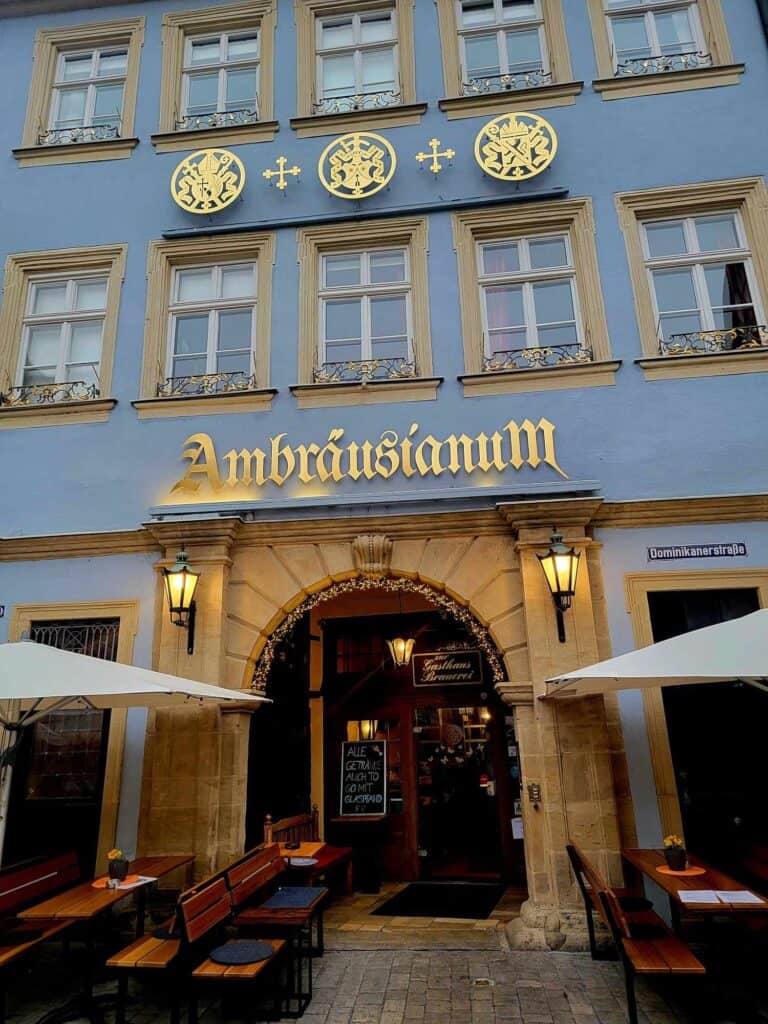 The blue facade of Ambrausianum with a gold calligraphy sign and a stone archway with lanterns on either side