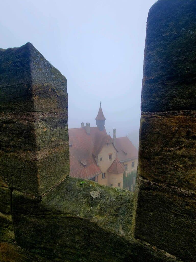 An orange colored castle with a red roof seen through the turrets of a tall tower