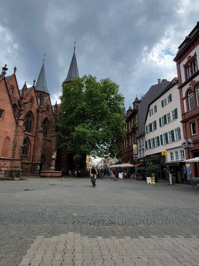 An open paved square in front. of Stiftskirche, with tables of restaurants and a bike rider