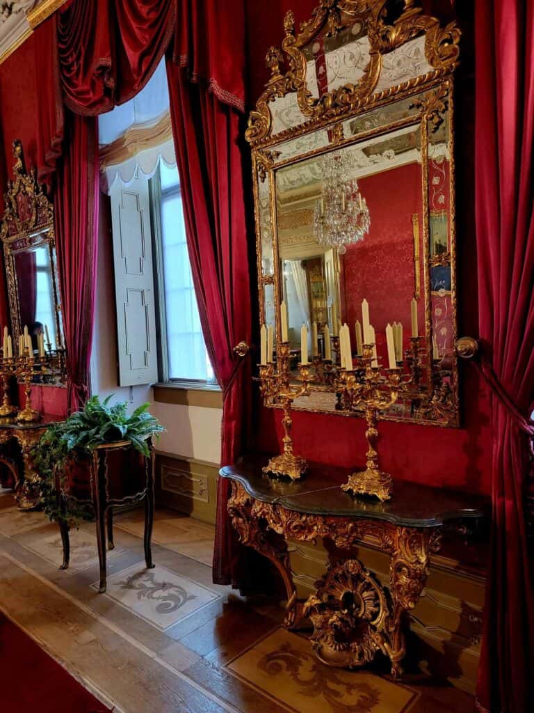 A lavishly decorated rococo room in red with red drapes and a gold table and mirror with candlesticks