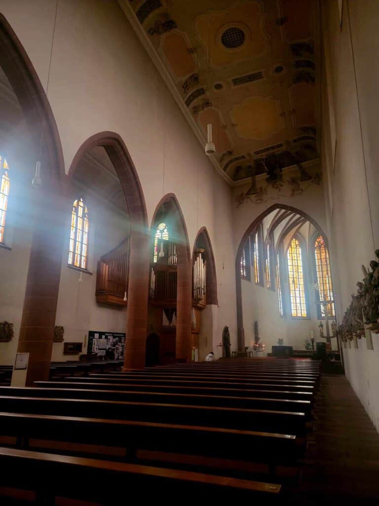 The inside of a church with arches and stained glass and wooden bench pews