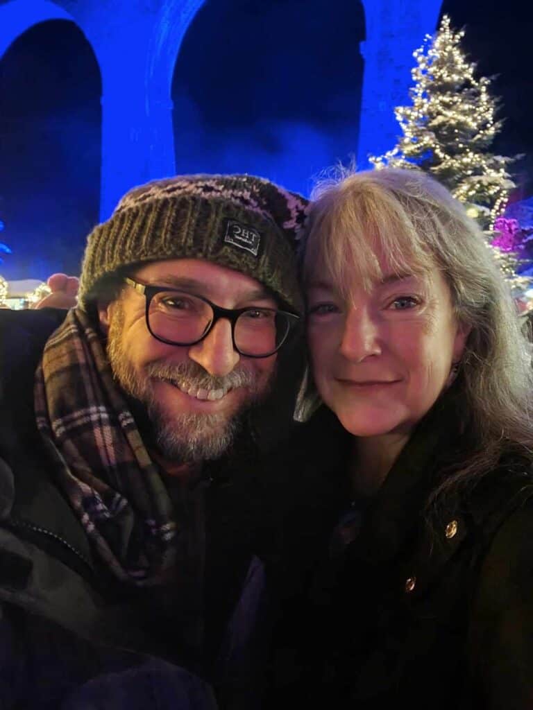 A smiling couple with a tall arched stone viaduct illuminated in blue behind