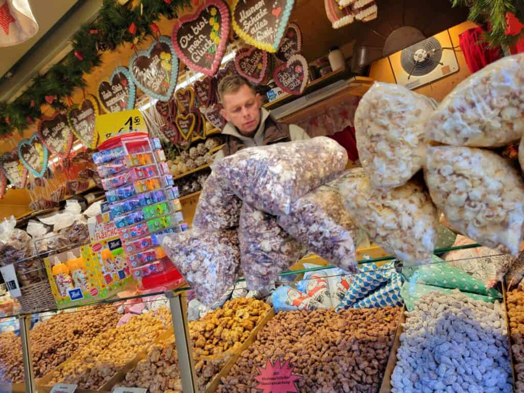 A christmas market stand filled with roasted candied nuts, bags of popcorn, and lebkuchen heart cookies