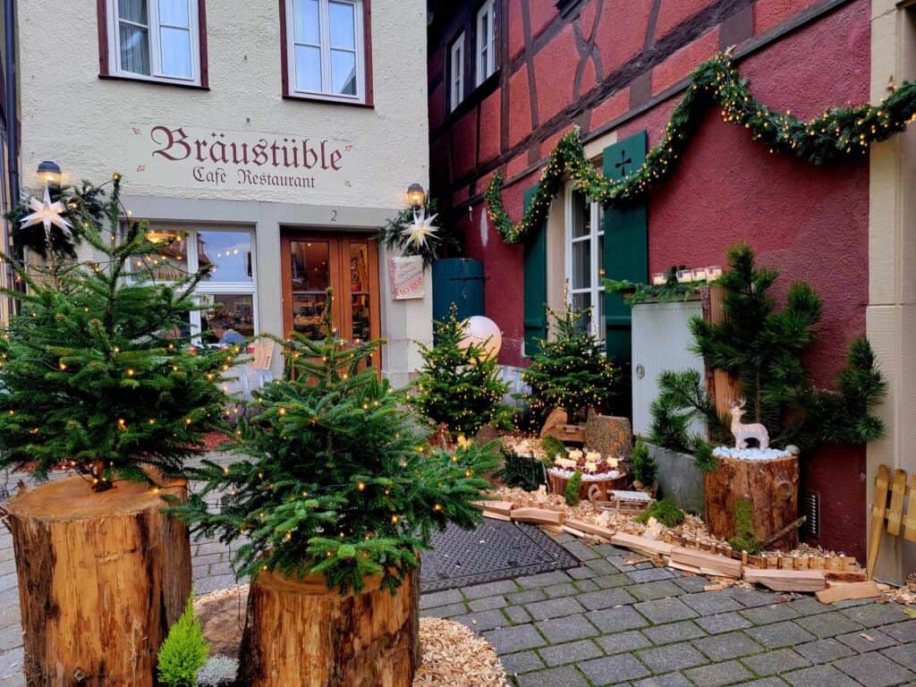 A cozy cafe with Braustuble cafe Restaurant painged on it, the courtyard in front is festively decorated in rustic Christmas style