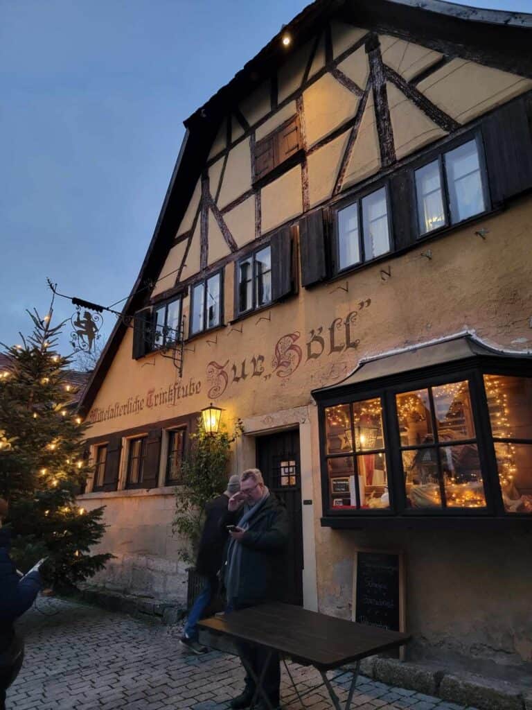 A very old looking medieval half timbered building with "Zur Höll" painted on the side in calligraphy and small white lights in the window