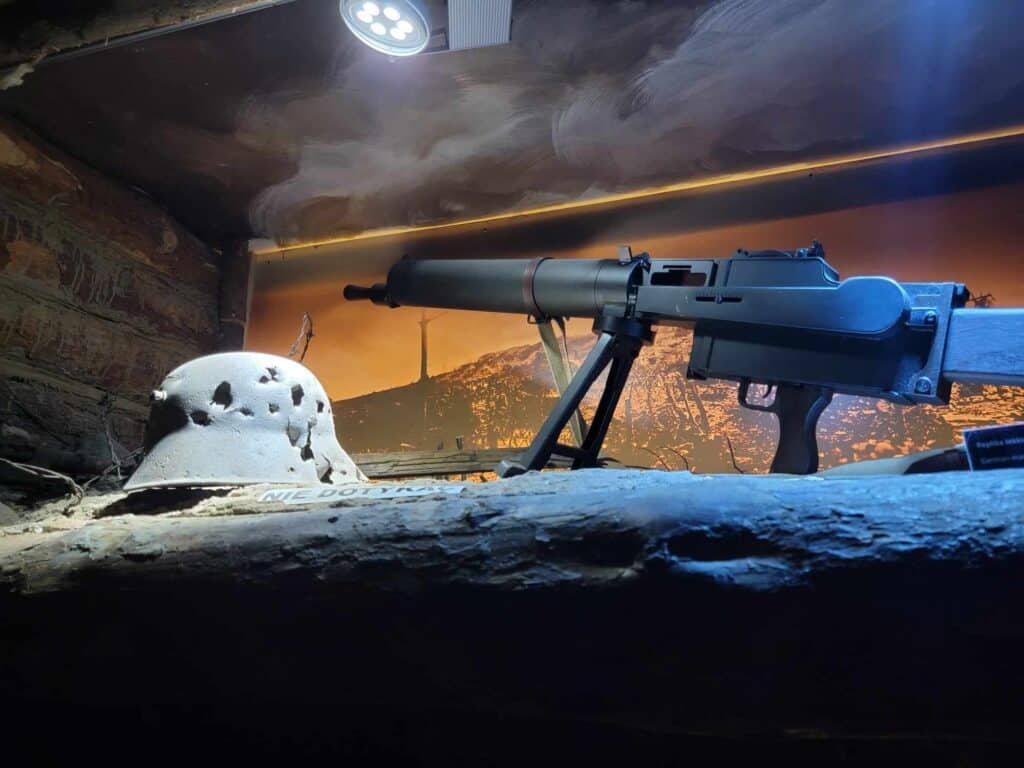 A long gun on a tripod and a world war 1 metal helmet shot full of holes in a display case