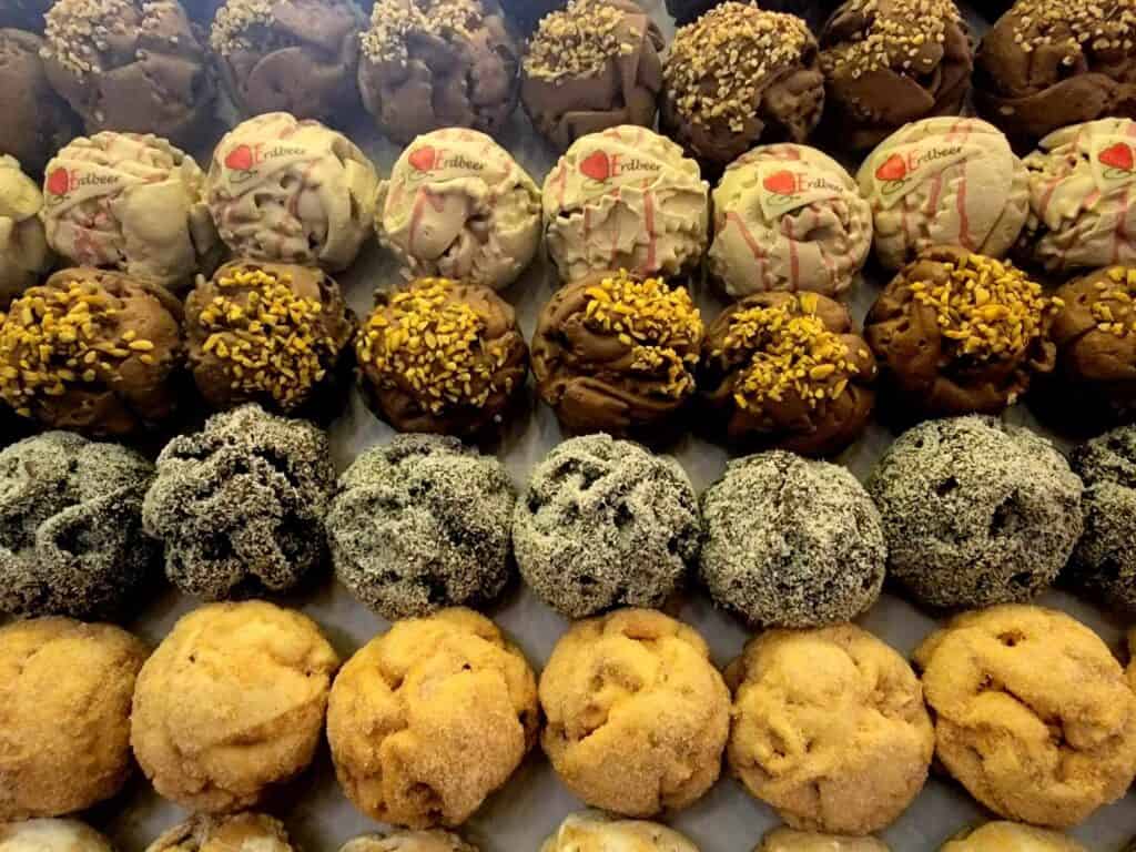 Rows of spherical schneeballen pastries covered in various glazes and sprinkled with sugar, coconut, and nuts