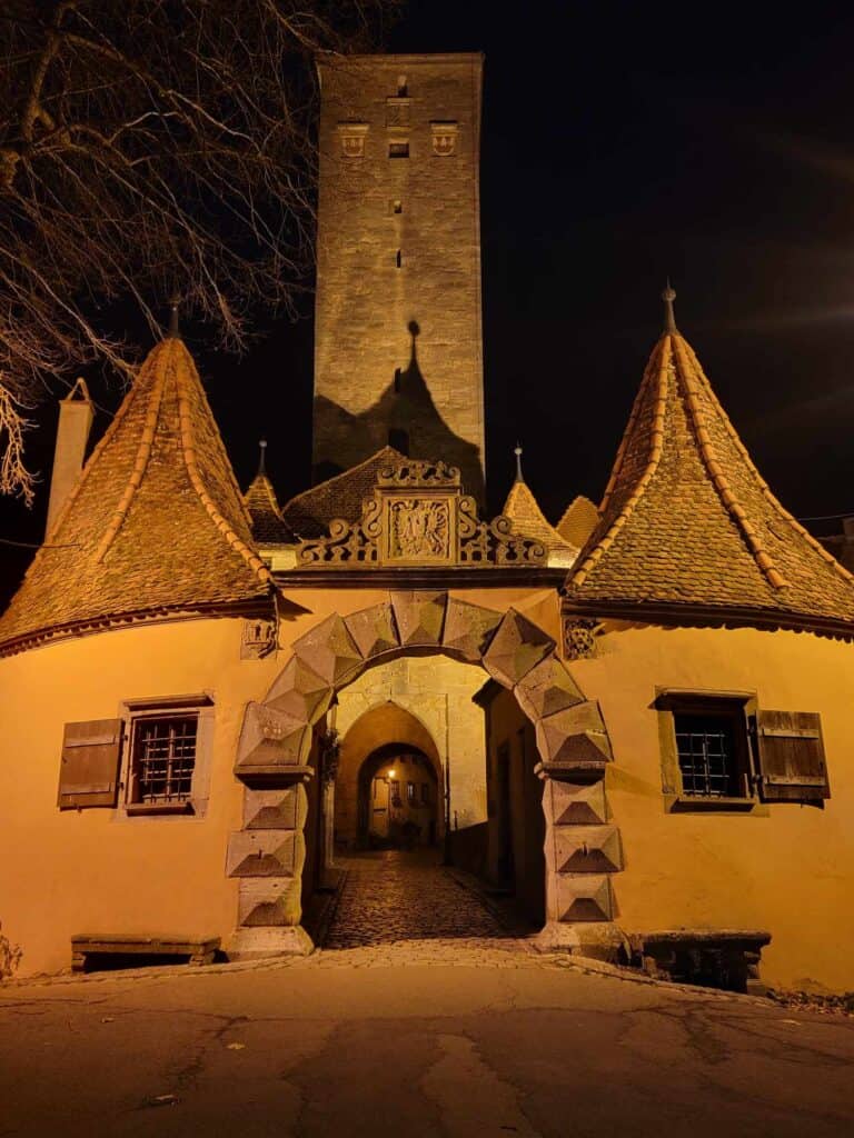 A medieval gate with pointed towers on either side lit up in a yellow glow at night