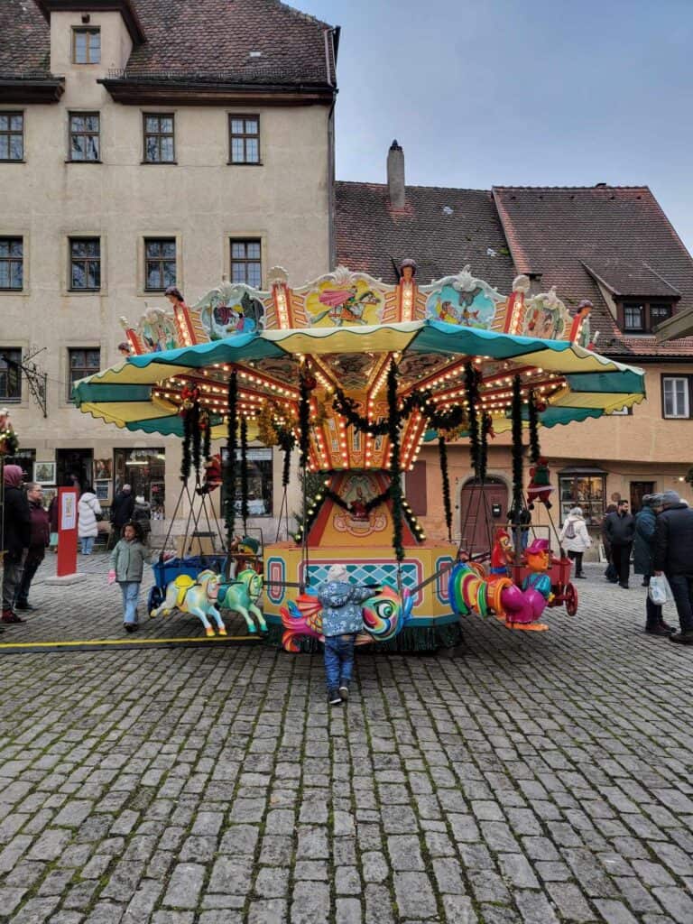 A small child stands back to the camera looking at a colorful vintage carousel