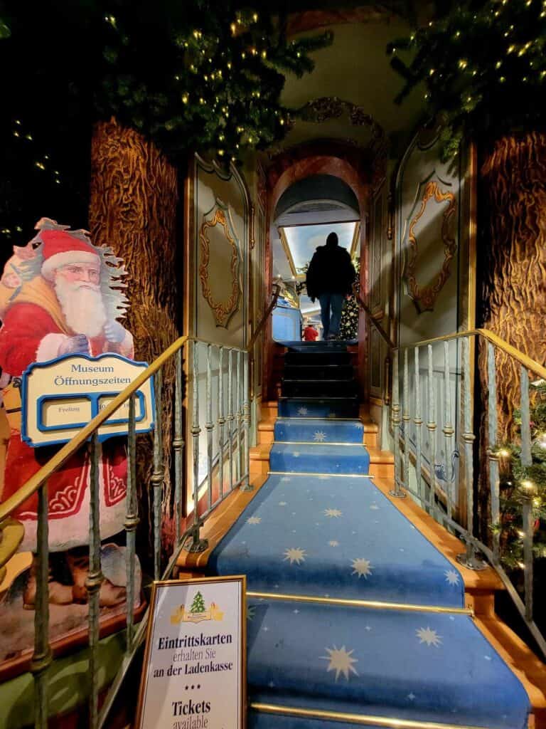 A man walks up blue carpeted stairs with stars, and a Santa cutout holds a sign with opening hours